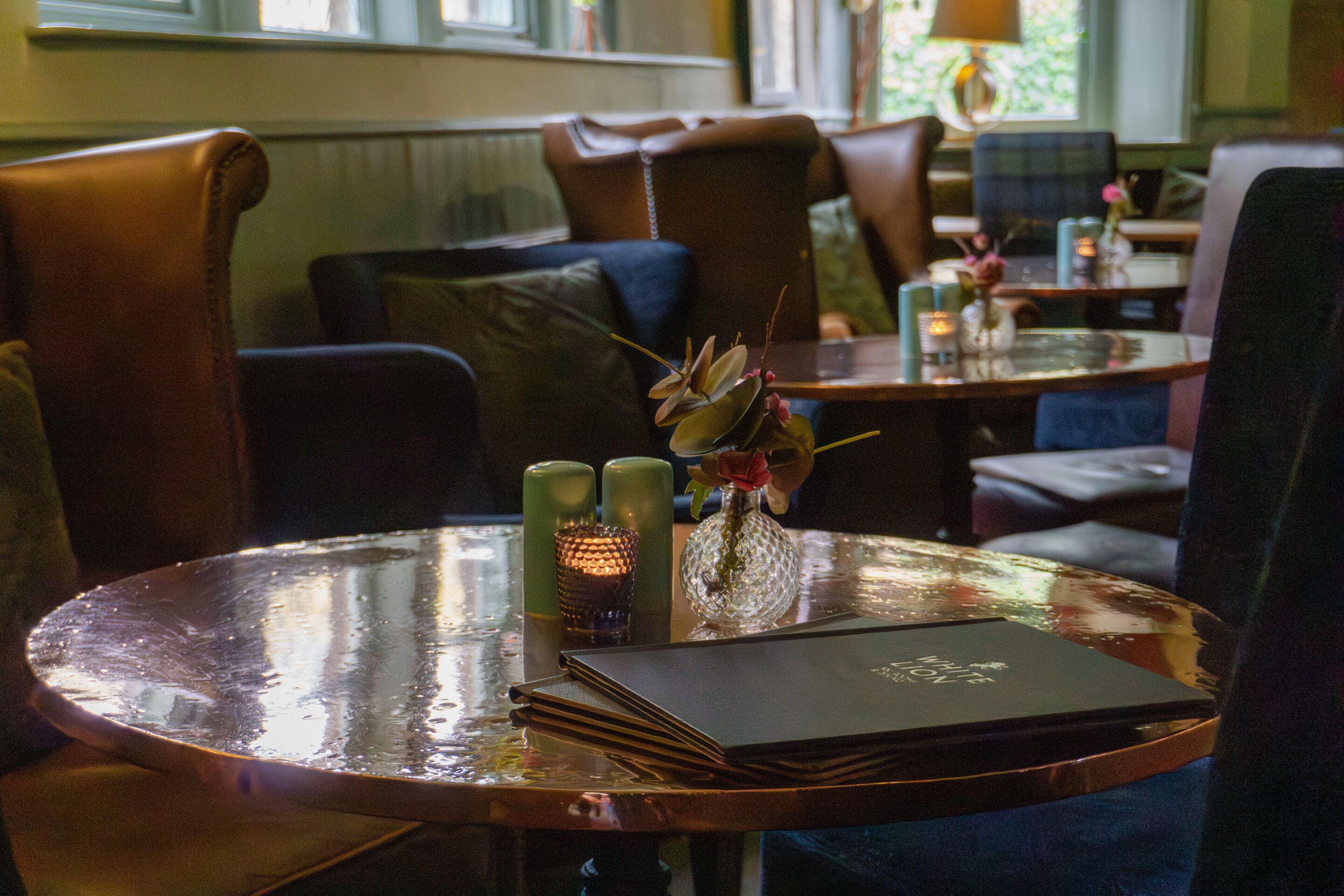A dining area with a round table, leather chairs, a vase with flowers, and candles.