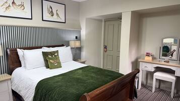 A hotel room with a bed, a desk, a chair, a lamp, and two framed pictures on the wall.