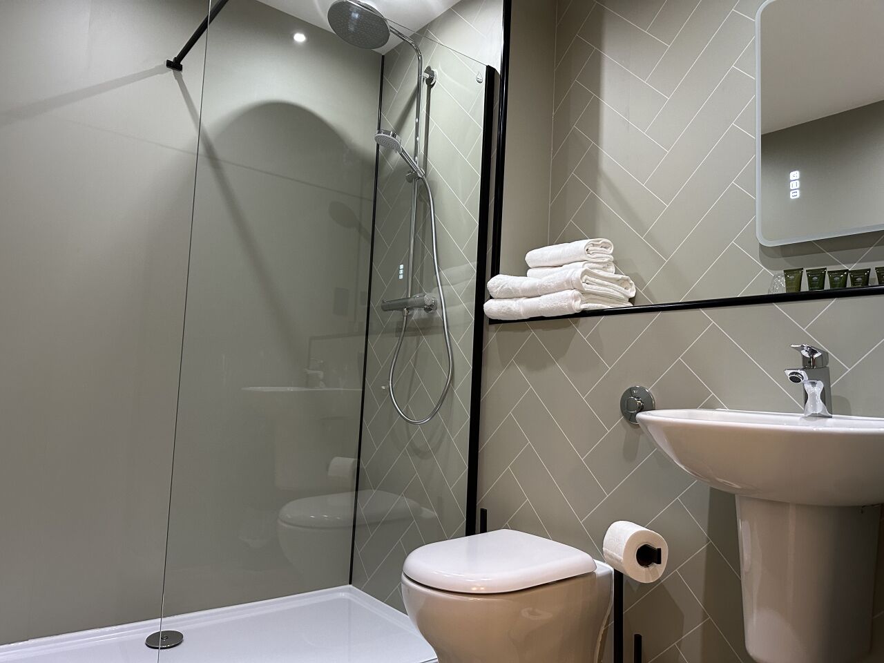 Un baño moderno con ducha de vidrio, inodoro blanco y lavamanos con espejo.