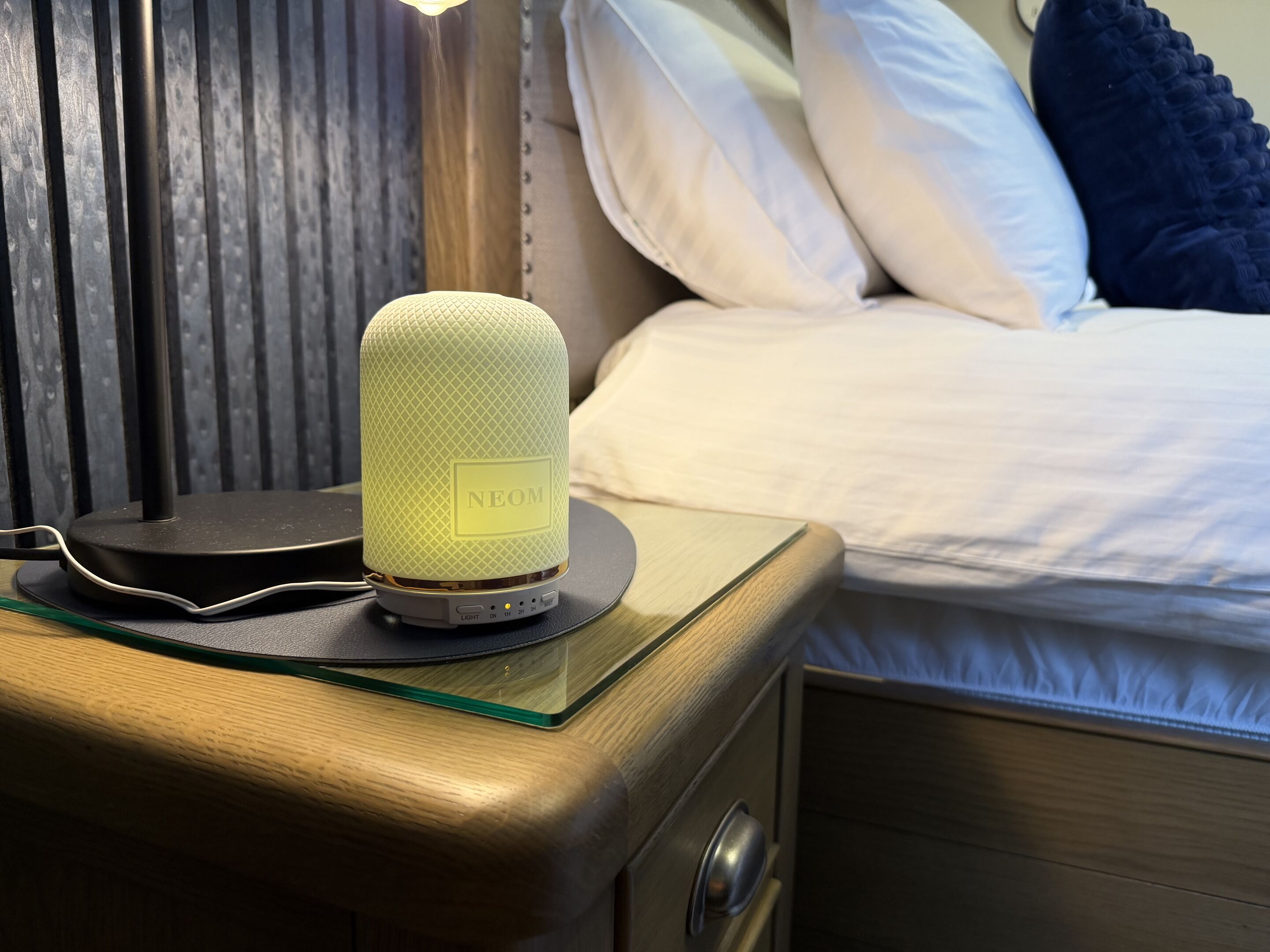 A bedside table with a speaker, a bed with pillows, and a wooden nightstand.