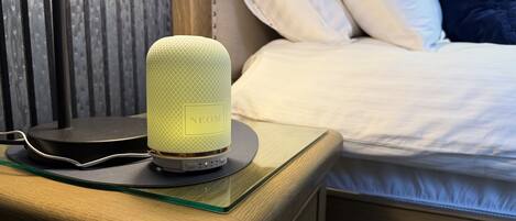 A bedside table with a speaker, a bed with pillows, and a wooden nightstand.