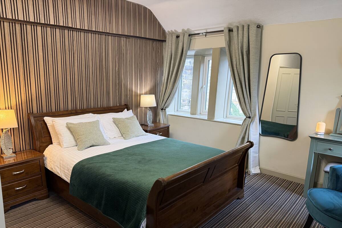 A neatly arranged hotel room with a wooden bed, a bedside table with a lamp, a dresser, and a mirror.