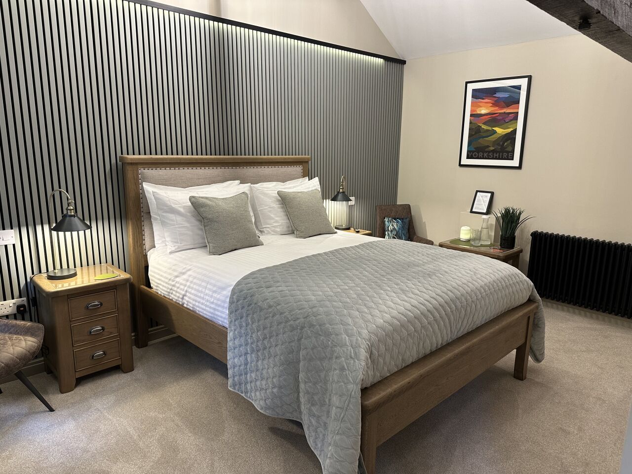 A bedroom with a wooden bed, a bedside table, a nightstand, a radiator, and a framed picture on the wall.