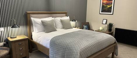 Un dormitorio con cama de madera, una mesita de noche, un radiador y un cuadro en la pared.