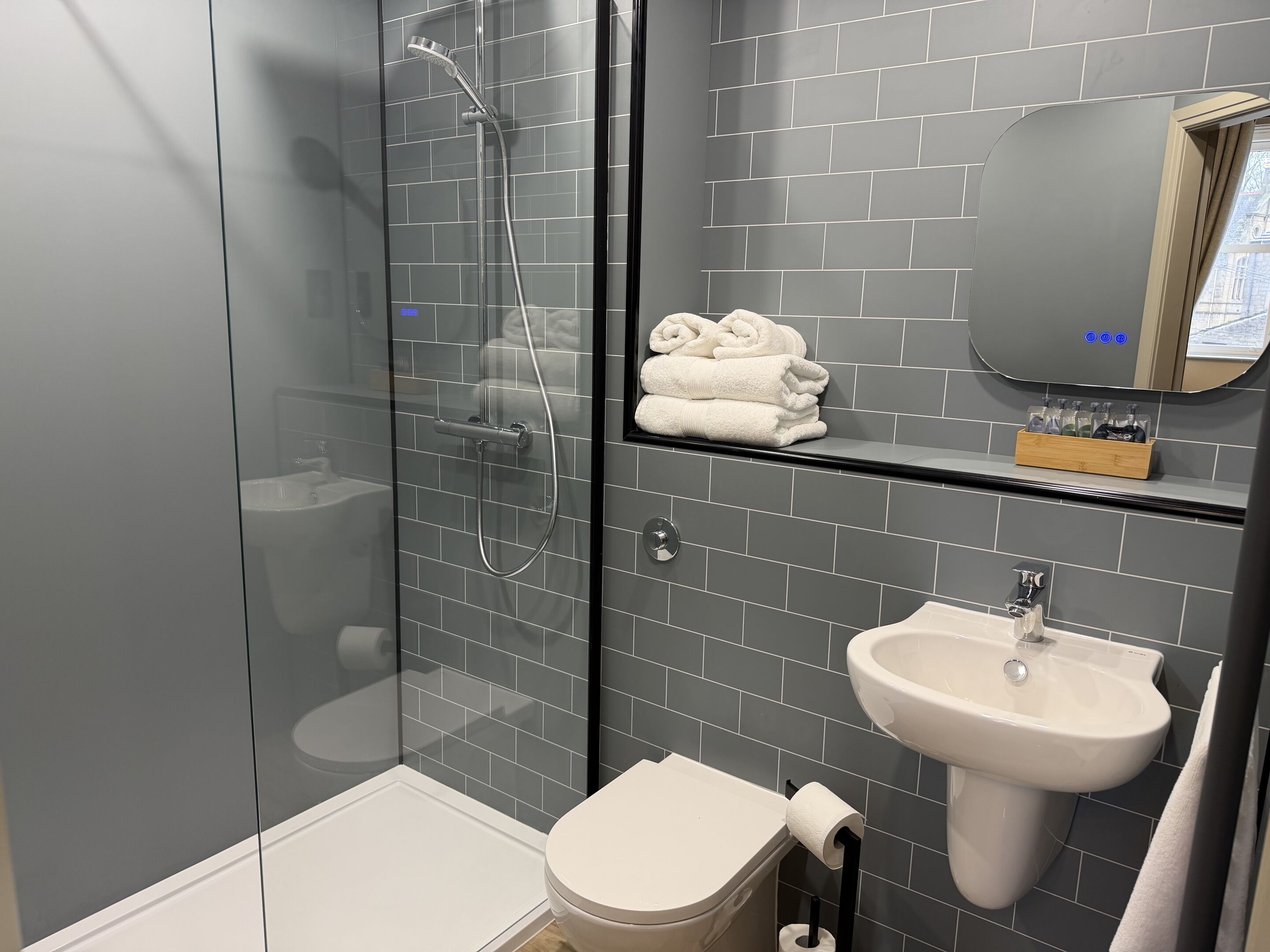 Un bagno moderno con doccia vetro, water, lavandino e specchio sopra il lavandino.