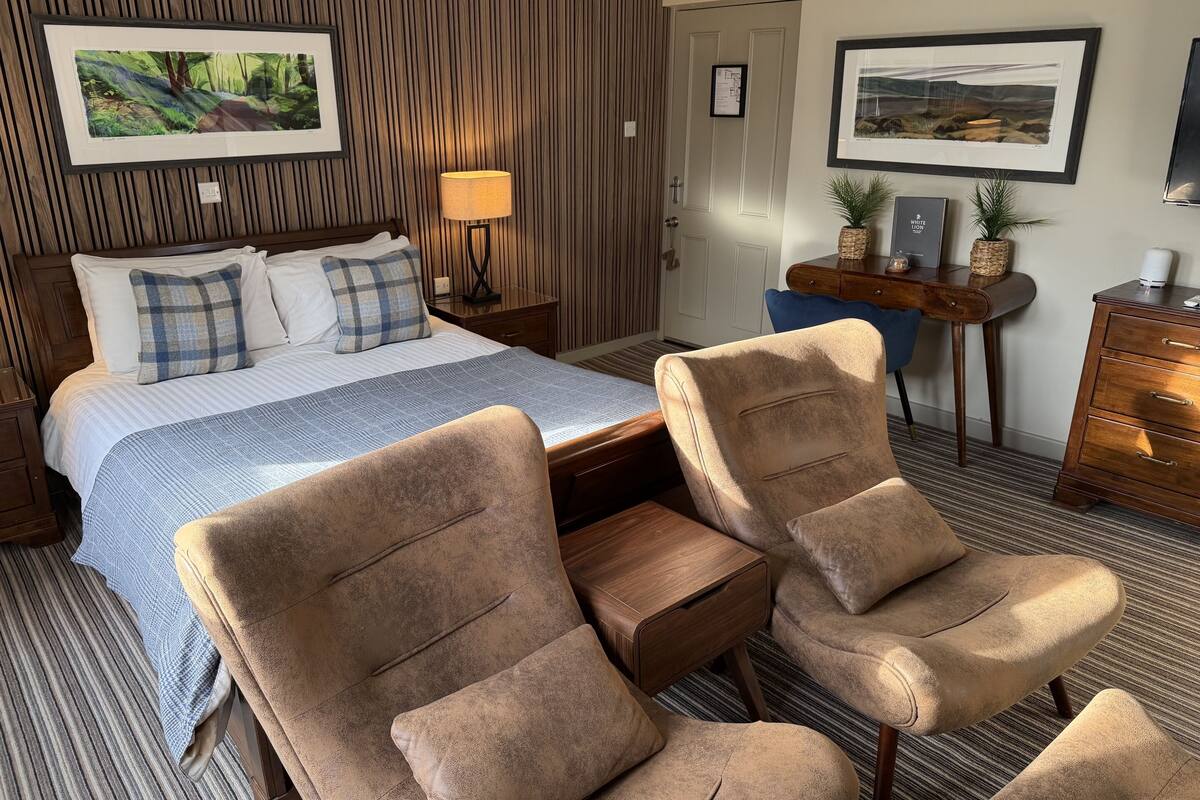 A hotel room with a bed, two armchairs, a desk, and a chair.