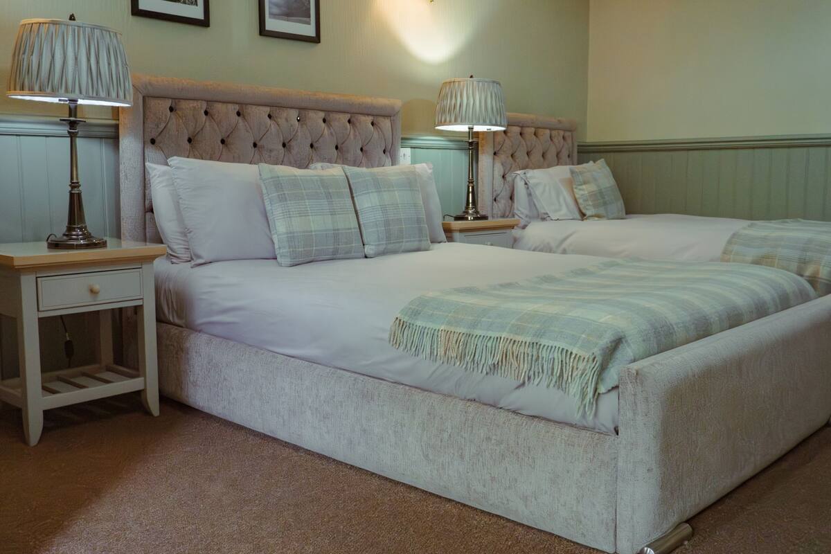 A double bed with a tufted headboard, two bedside tables with lamps, and a plaid throw blanket.