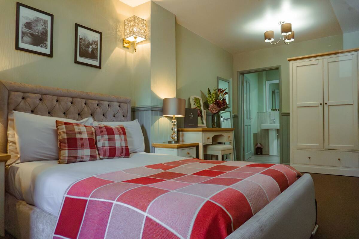 A neatly arranged bedroom with a large bed, bedside tables, a dresser, and a wardrobe.