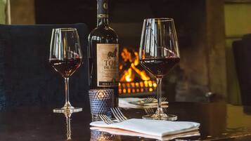 A bottle of wine, two wine glasses, and a glass of water on a table with a fireplace in the background.