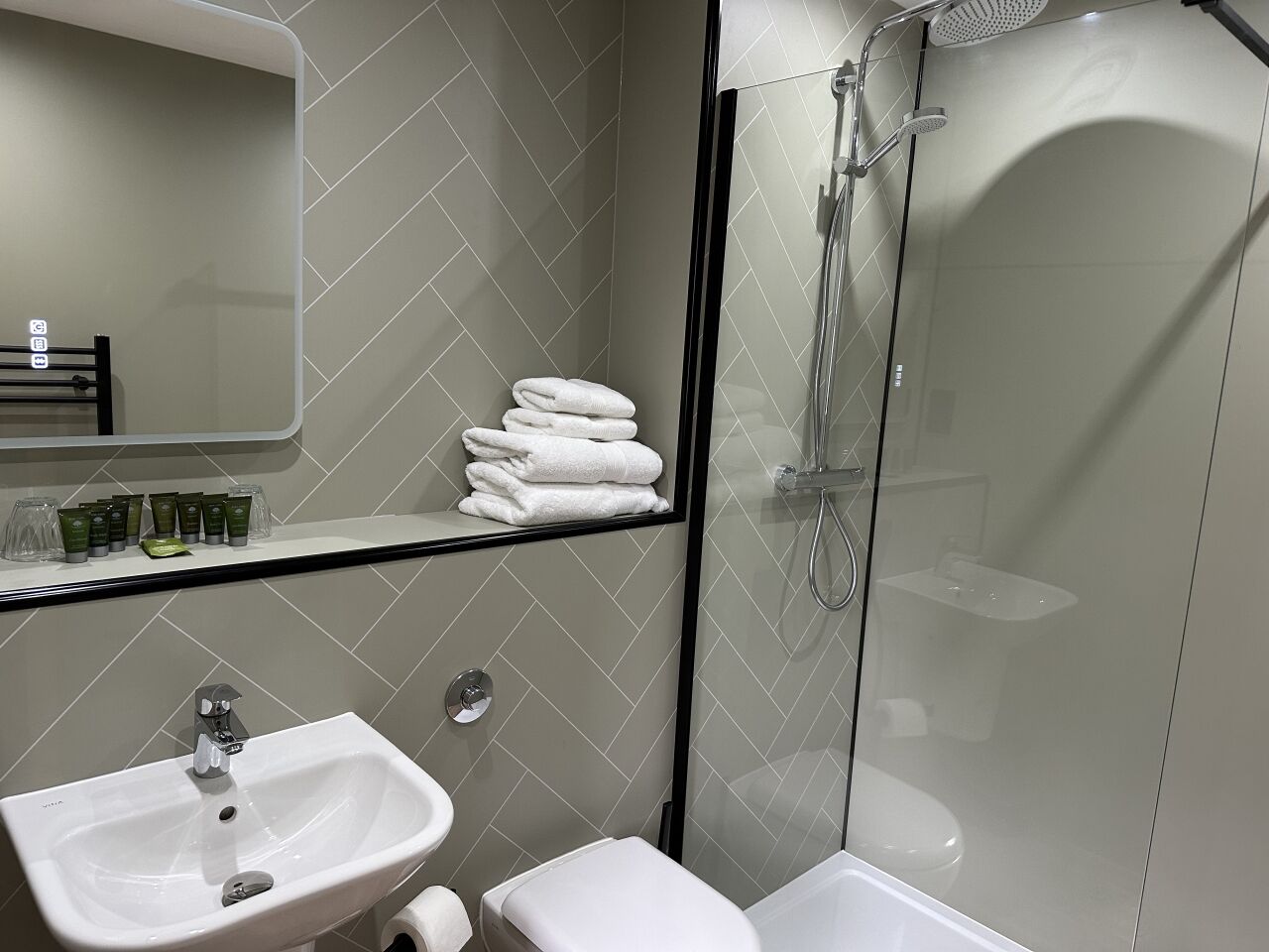 Un baño moderno con cabina de ducha de vidrio, un lavabo blanco y un inodoro.