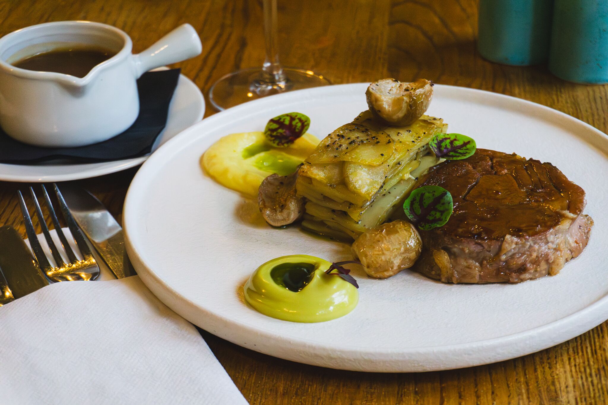 A plate of food with a steak, potatoes, and a green sauce.