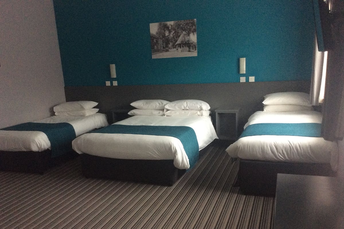 A hotel room with three beds, a small table, and a wall-mounted picture.
