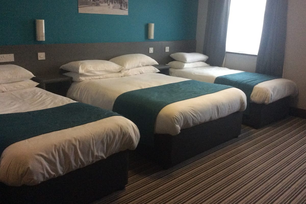 A hotel room with three single beds, a teal accent wall, a framed picture, and a window with curtains.