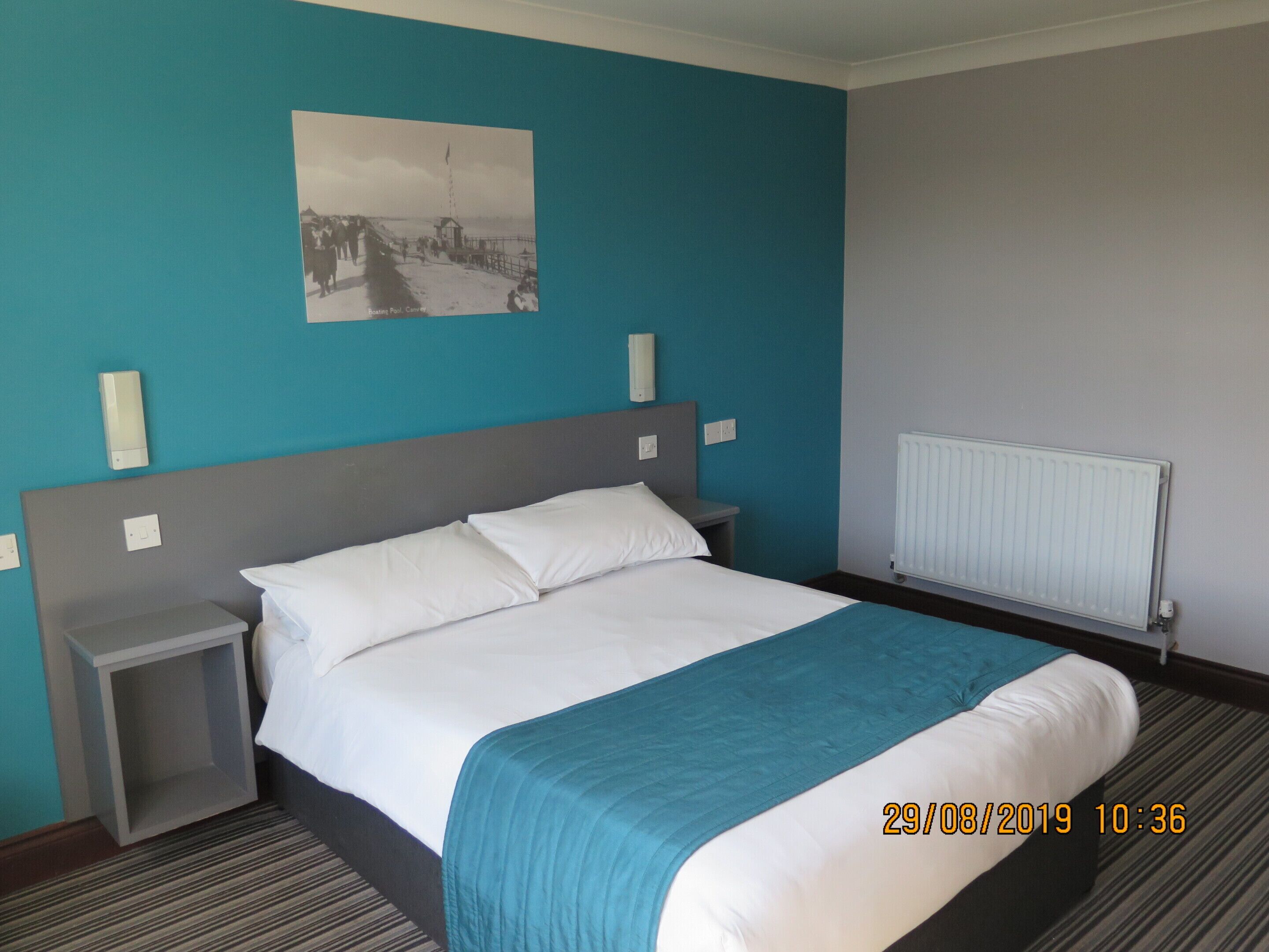 Ein Hotelzimmer mit einem Bett, einem Nachttisch, einem Bild an der Wand und einer Heizung.