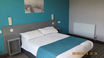 A hotel room with a bed, a nightstand, a picture on the wall, and a radiator.