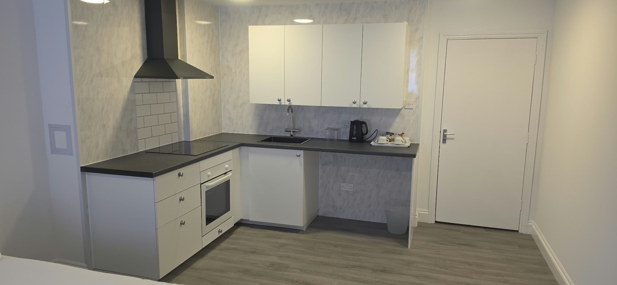 A compact kitchen with a built-in oven, a sink, and a black range hood.