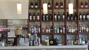 Un espace bar avec des étagères remplies de bouteilles de vin, un lustre et une personne derrière le comptoir.