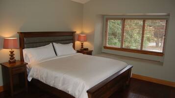 A neatly made bed with white linens, two bedside lamps, and a window with blinds.