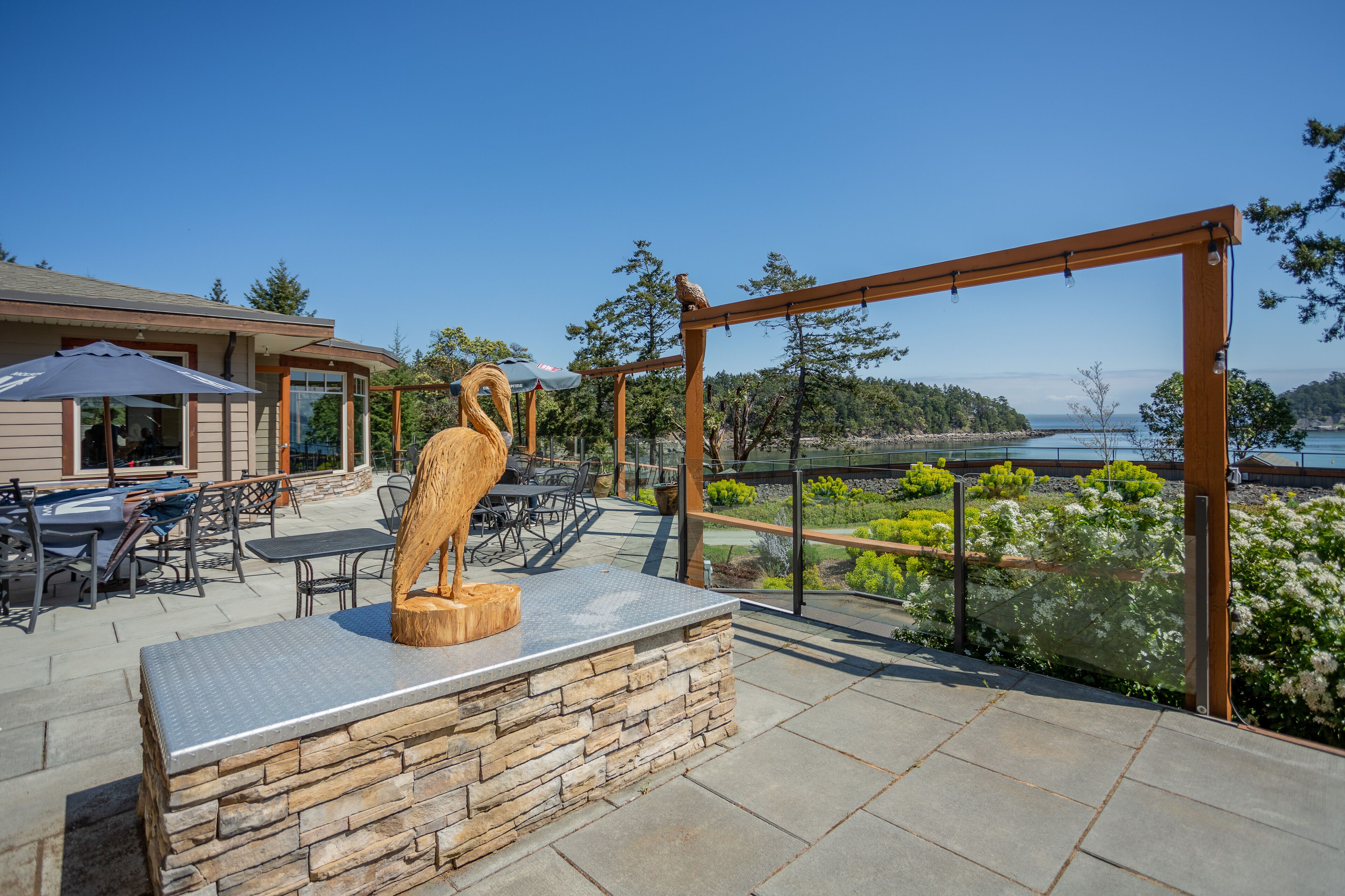 An outdoor patio with stone seating, a wooden sculpture, and a view of a lake.