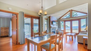 A spacious living area with a wooden dining table, comfortable seating, and large windows offering ocean views.