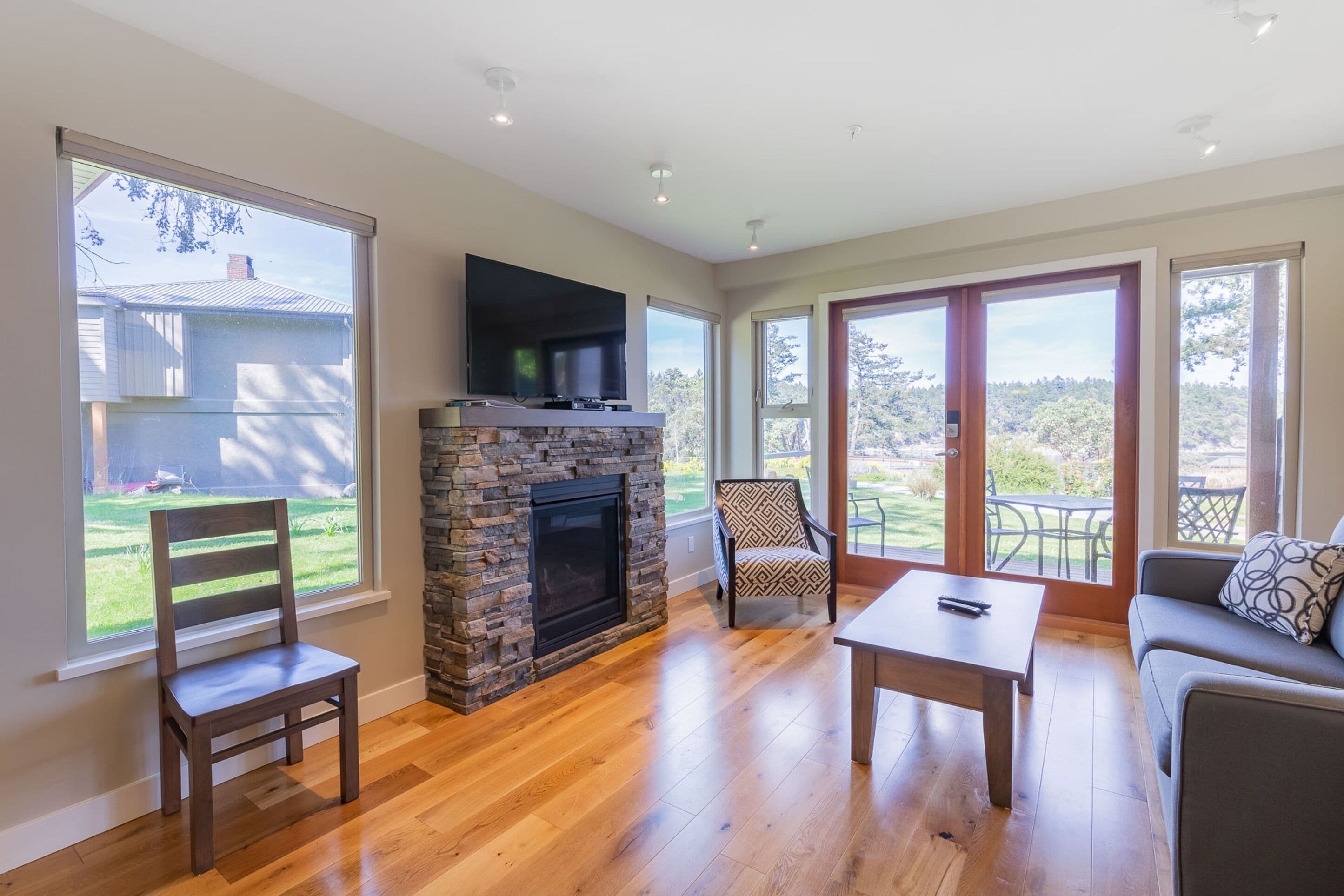 A spacious living room with a stone fireplace, a flat-screen TV mounted above it, and a large sliding glass door leading to an outdoor patio.