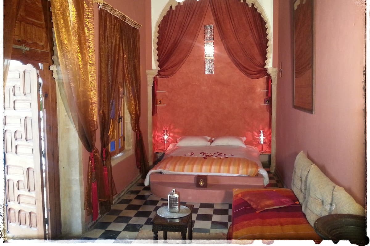 A room with a bed, a sofa, a small table, and a decorative mirror.