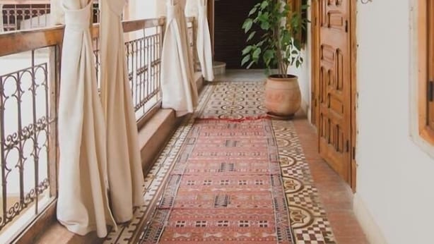 Un pasillo con alfombra estampada, cortinas blancas y una planta en maceta.