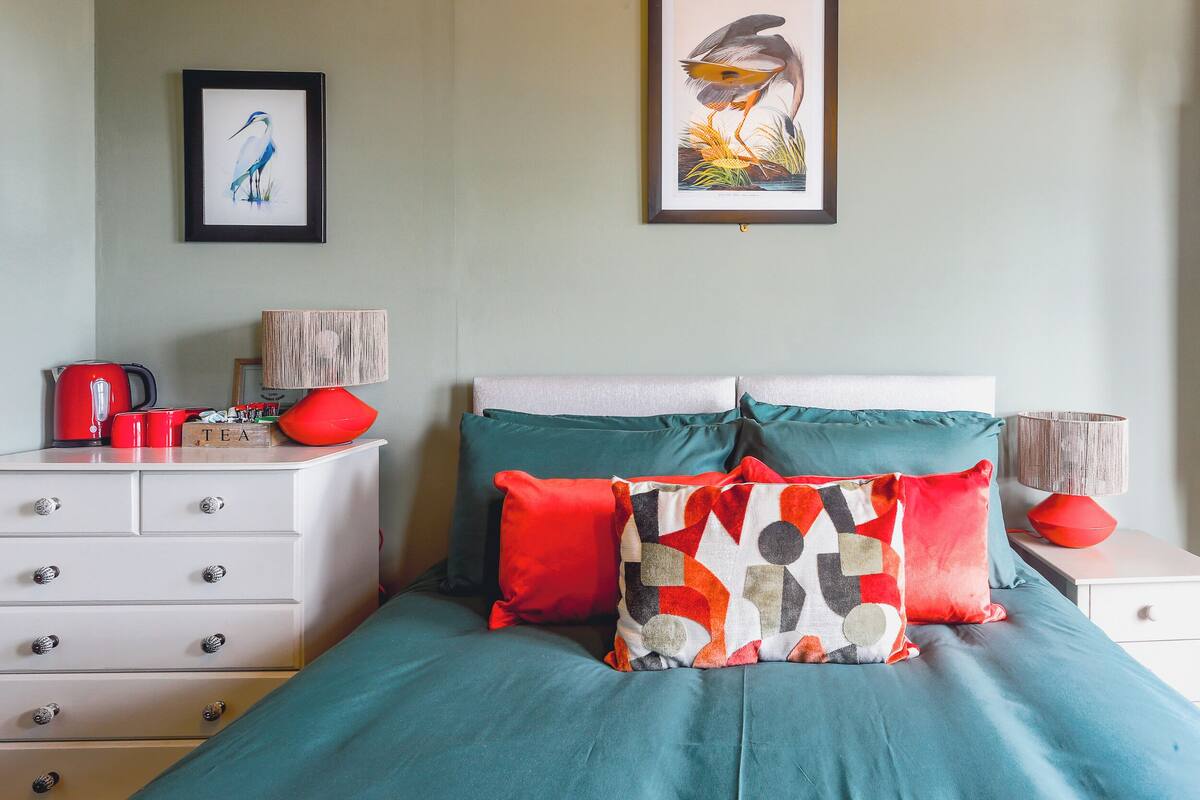 Una camera da letto ordinata con un letto, cuscini, una cassettiera, un comodino e due quadri appesi al muro.