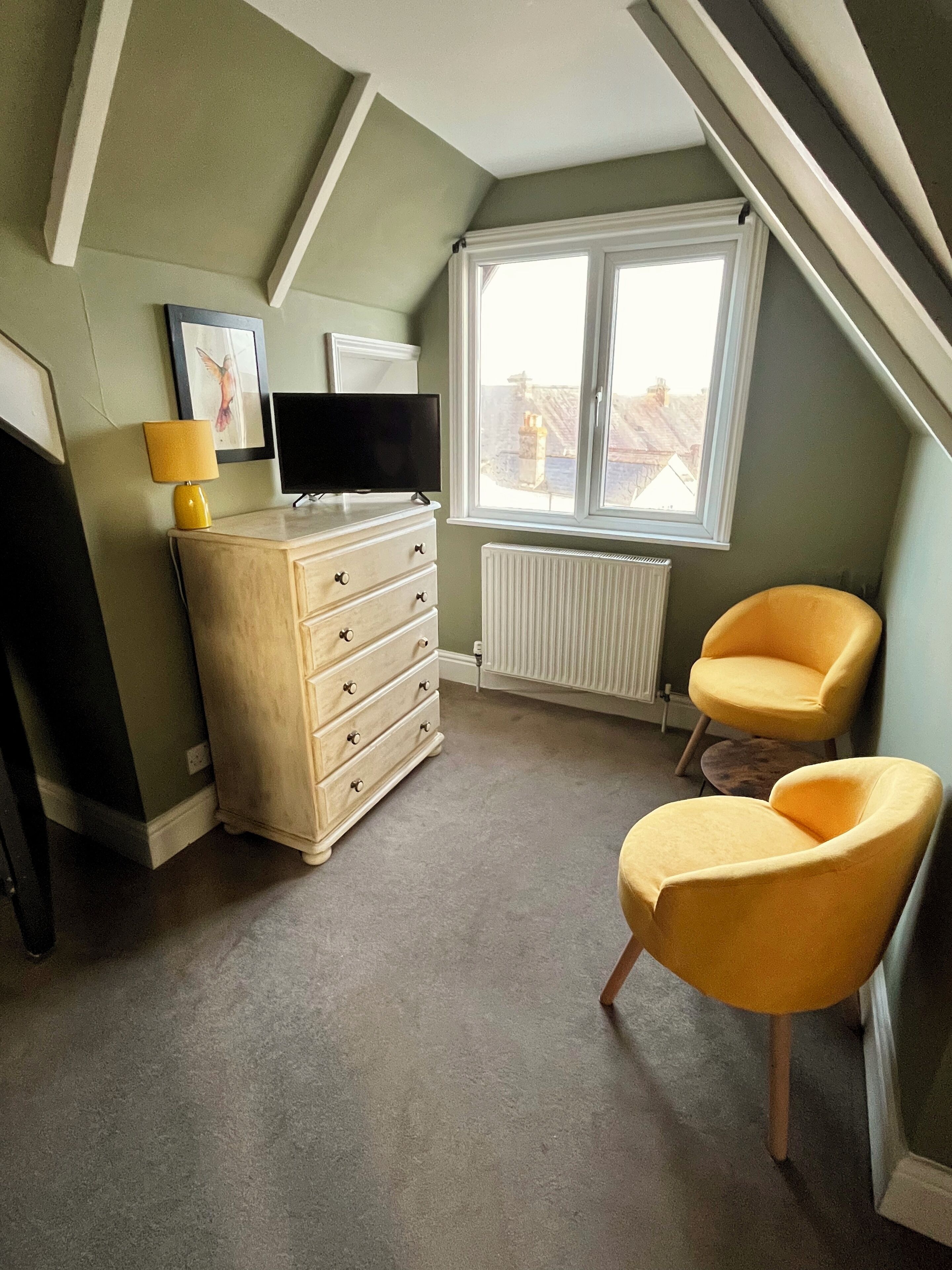 A room with a dresser, a television, two yellow chairs, a window, and a radiator.