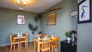 A dining area with a wooden table and chairs, a coffee machine, and wall decorations including a framed map and a framed bird illustration. - Smarties Guest House (Newquay)