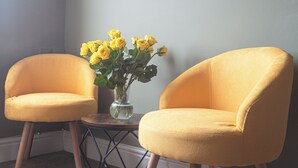 A room with two yellow armchairs, a small table with a vase of yellow flowers, and a sloped ceiling with white trim. - Smarties Guest House (Newquay)