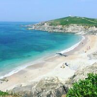 Uma praia com águas turquesa cristalinas, areal arenoso e falésias rochosas.
