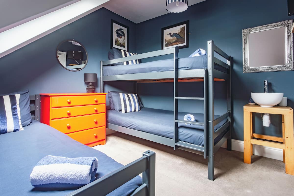 Un letto a castello con una scala in legno, un comò rosso, uno specchio rotondo e un piccolo sgabello di legno con un lavandino.