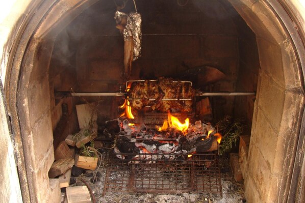 A traditional wood-fired oven with burning wood and a rack of meat.