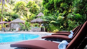 A poolside area with lounge chairs, a stone structure, and thatched umbrellas.