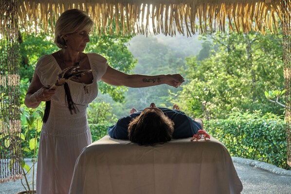A person lying on a massage table outdoors, with a natural backdrop of trees and hanging decorations. - Luna Lodge (Puerto Jiménez)