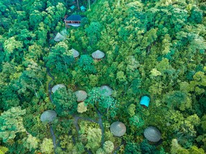 An aerial view of a forested area with several thatched-roof structures, likely accommodations, amidst dense greenery. - Luna Lodge (Puerto Jiménez)