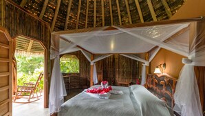 A room with a bed, a rocking chair, and a view of greenery outside.