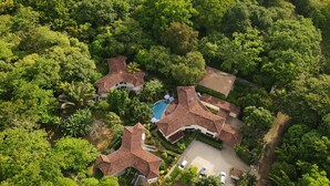 Vista aérea de un complejo turístico con varias construcciones, piscina y exuberante vegetación.