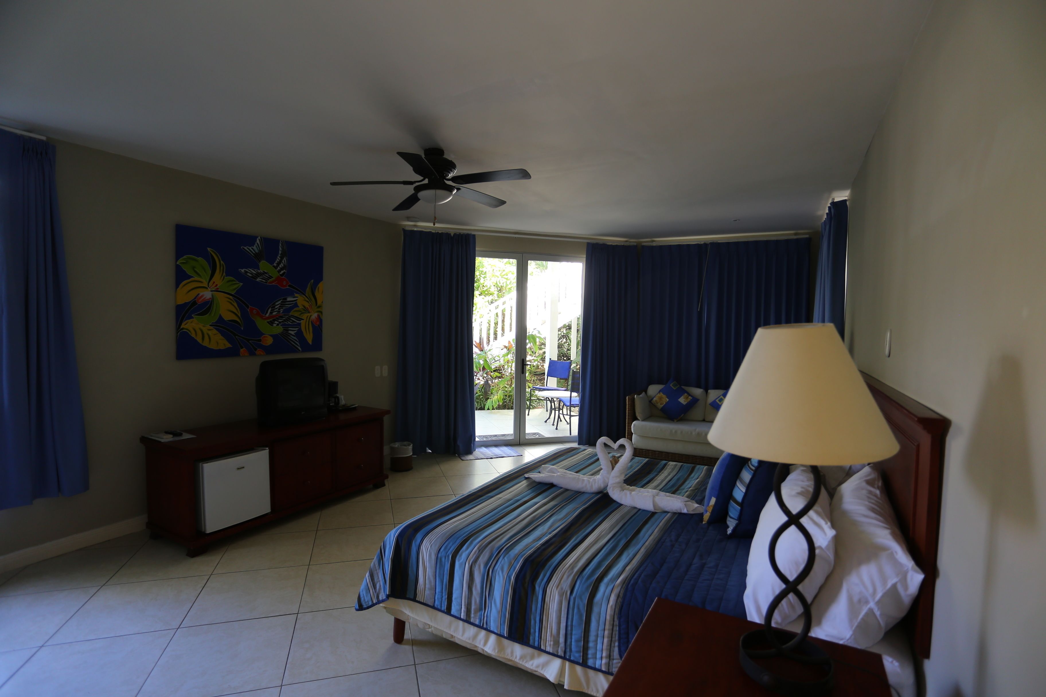 A hotel room with a bed, a desk, a television, a ceiling fan, and a window with curtains.