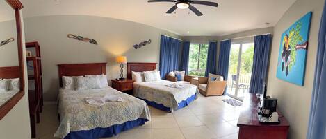 A hotel room with two beds, a desk, a chair, a ceiling fan, and a view of the outdoors.