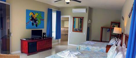 A hotel room with two beds, a TV, a ceiling fan, and a painting on the wall.