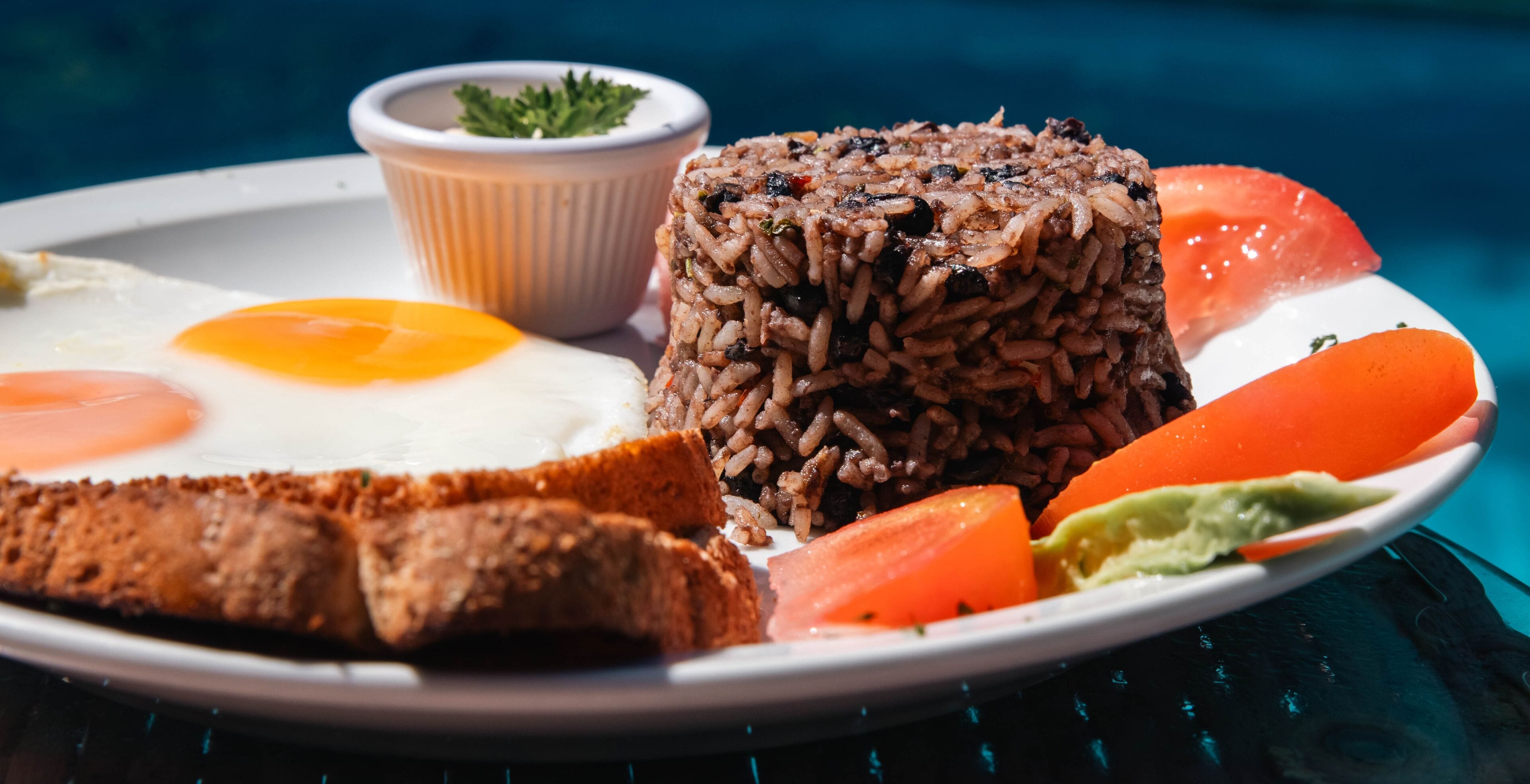 Un plato con un huevo frito, una porción de arroz, rebanadas de pan y tomate.