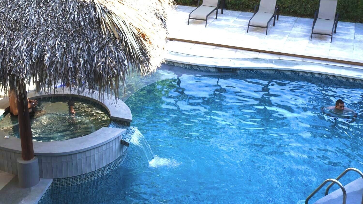 A swimming pool with a hot tub and a waterfall feature.