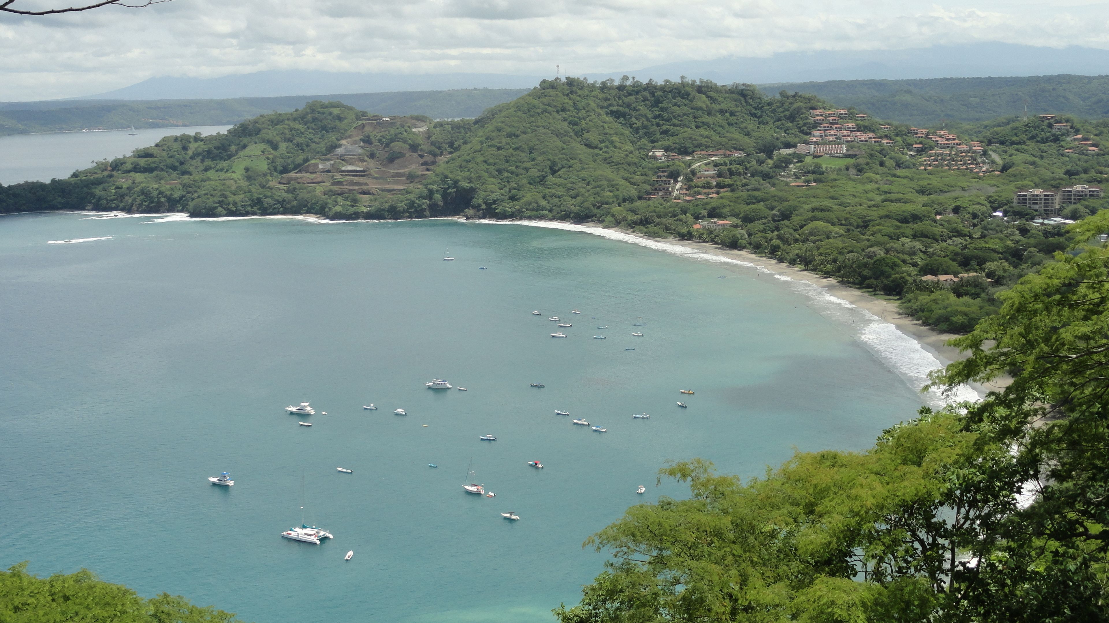 A coastal area with boats on the water, a beach, and buildings on a hillside.