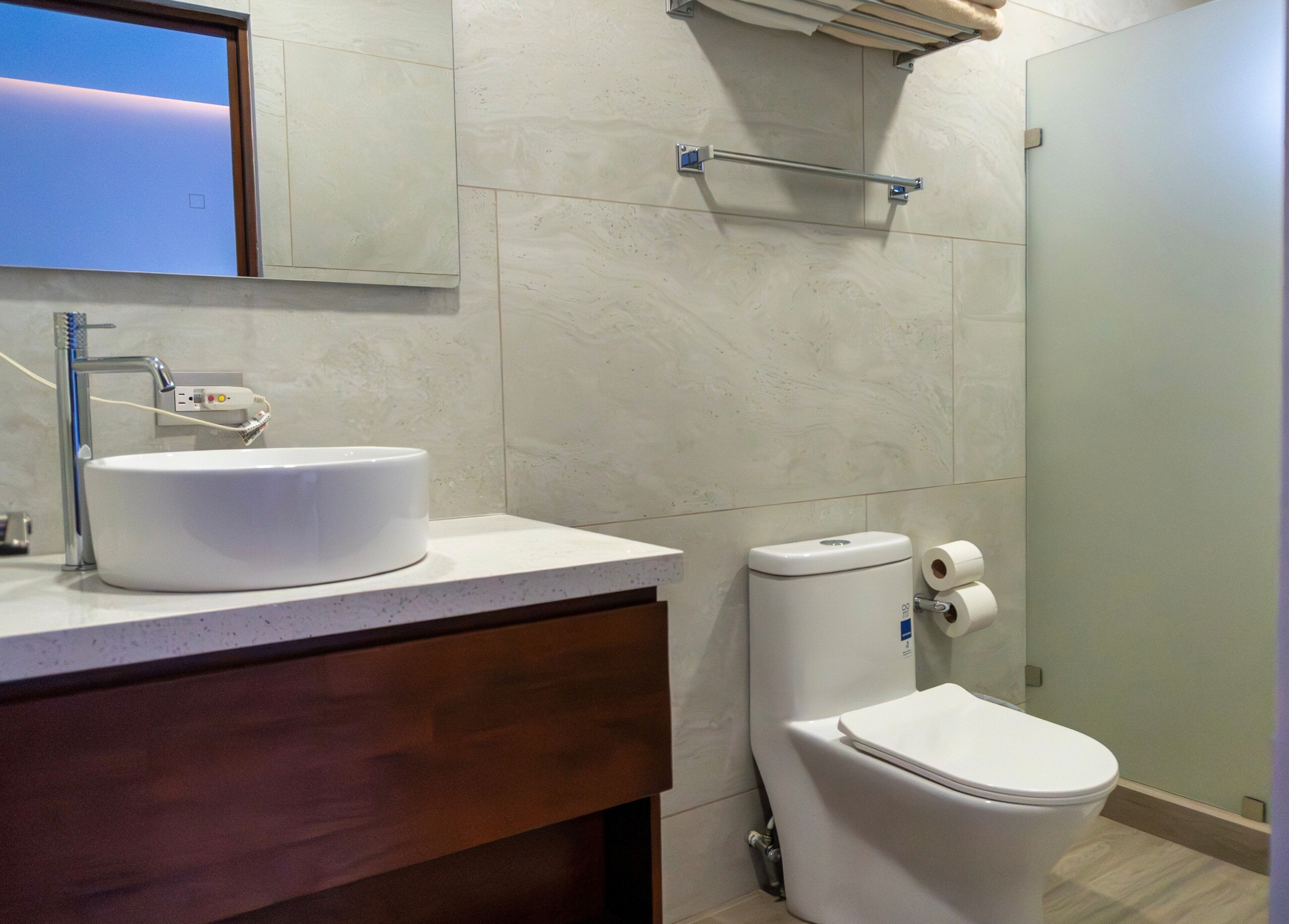Une salle de bain moderne avec un lavabo blanc, des toilettes et un porte-serviettes placé au-dessus des toilettes.