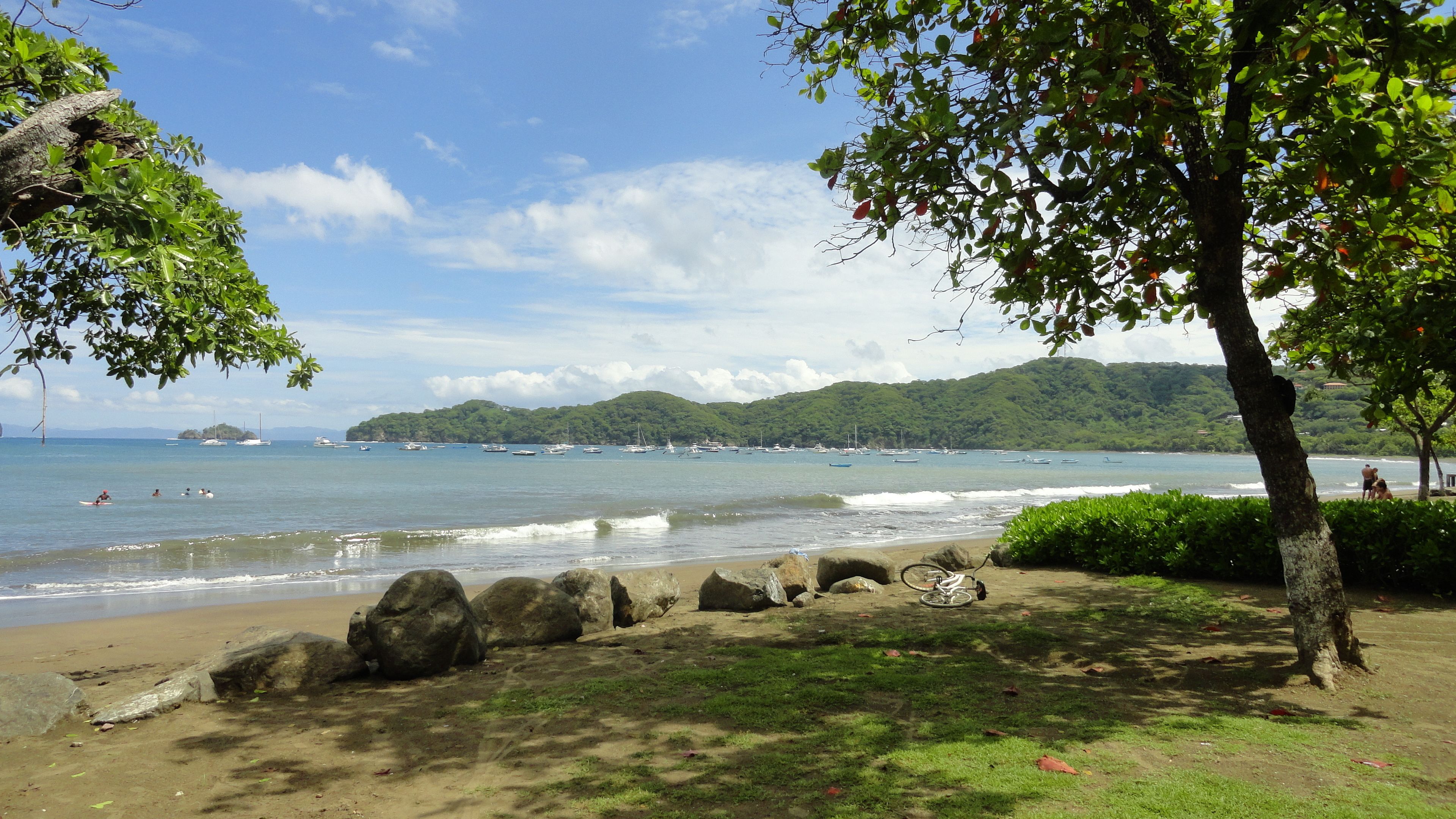 A beach with a rocky shoreline, a bicycle, and a view of boats on the water.