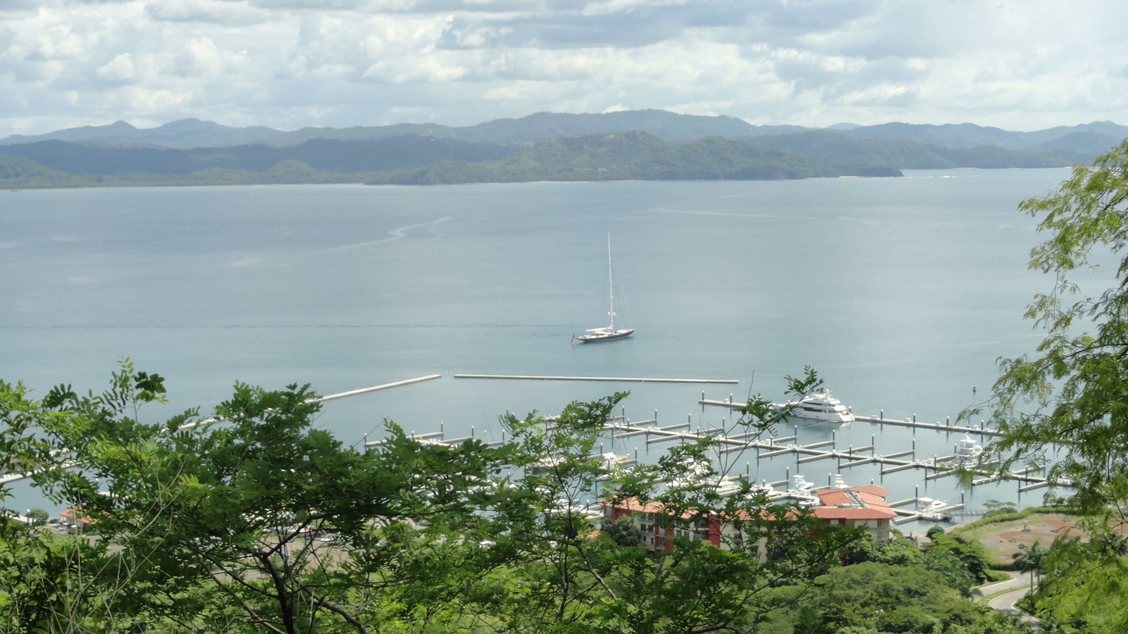 A marina with boats docked, surrounded by lush greenery and mountains in the background.