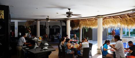An outdoor dining area with thatched roofs, tables, and chairs.