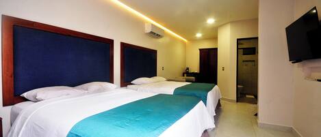 A hotel room with two beds, a TV mounted on the wall, and a bathroom visible through an open door.